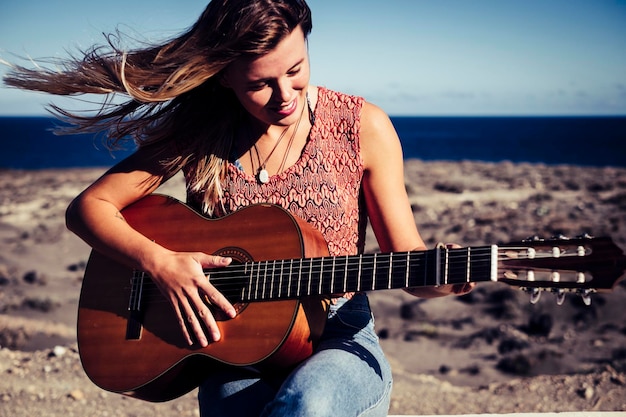 smiling young woman playing guitar at beach