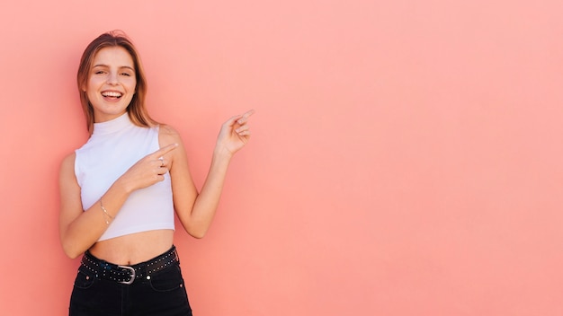 Photo smiling young woman pointing fingers against peach colored backdrop