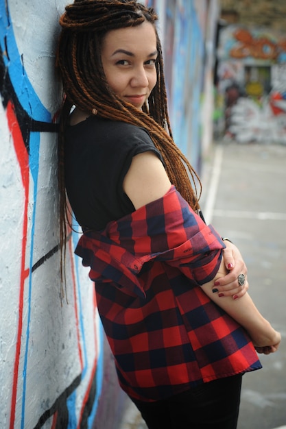 Photo smiling young woman portrait with dreadlocks, against graffiti