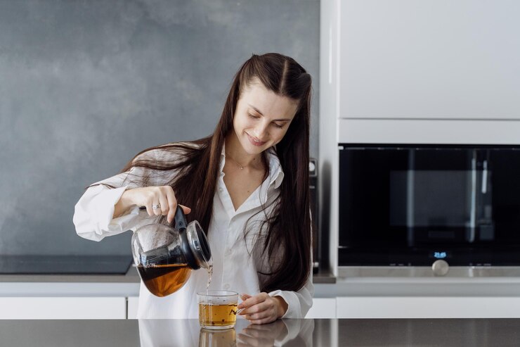 Smiling young woman pouring herbal tea in cup