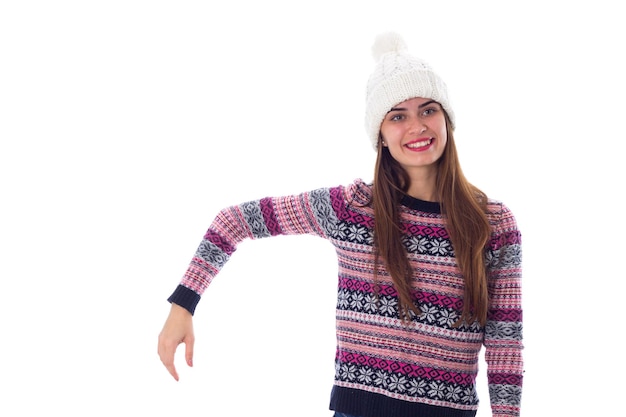 Smiling young woman in purple sweater and white hat holding something on white background in studio