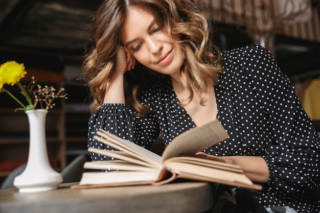 Smiling young woman reading book while sitting at the cafe