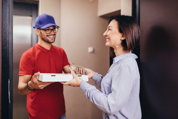 Smiling young woman receiving pizza from delivery man at home.