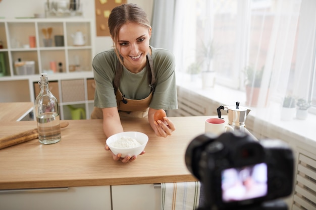 Smiling young woman showing the recipe while shooting a cooking video in the kitchen