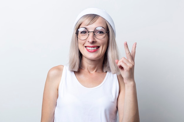 Smiling young woman showing two fingers a victory sign on a light background.