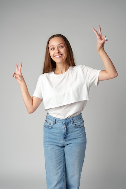 Smiling young woman showing victory sign on gray background