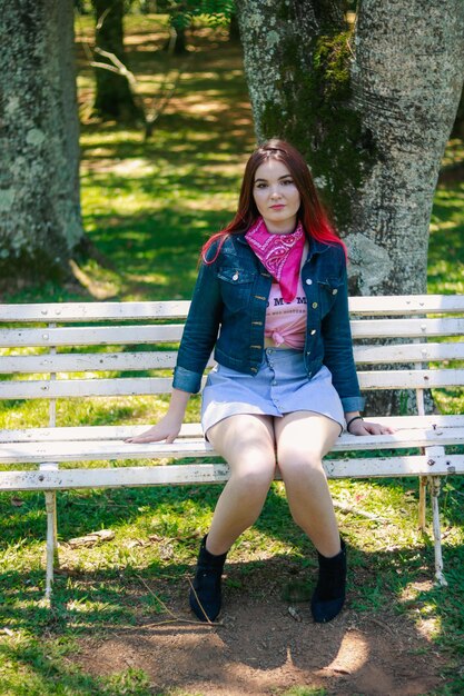 Photo smiling young woman sitting on bench in park