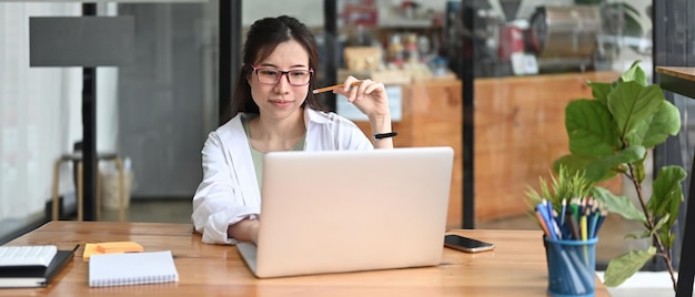 Улыбающаяся молодая женщина сидит в кафе и работает с ноутбуком