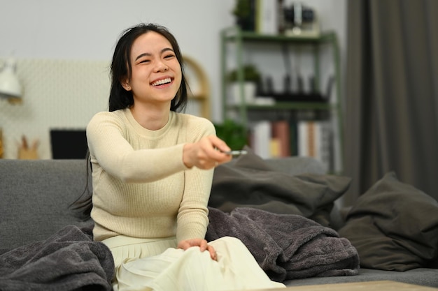 smiling young woman sitting on the couch and watching tv entertainment and hobby concept
