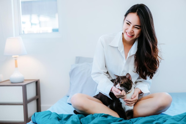 家でベッドに猫と一緒に座っている笑顔の若い女性