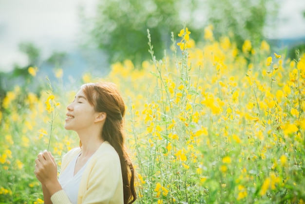 写真 畑で黄色い花がく植物のそばに立っている笑顔の若い女性