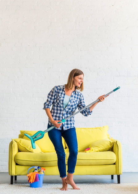 Smiling young woman standing on carpet dancing with mop