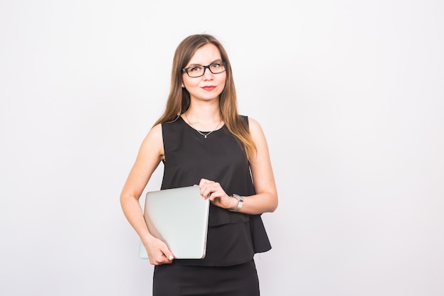 Smiling young woman standing and holding laptop over white background.