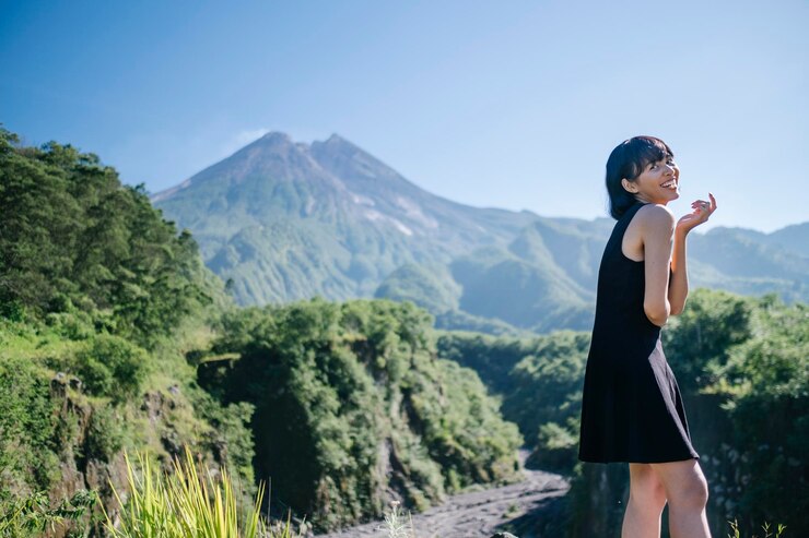 Photo 笑顔の若い女性が山と空に逆らって地面に立っています