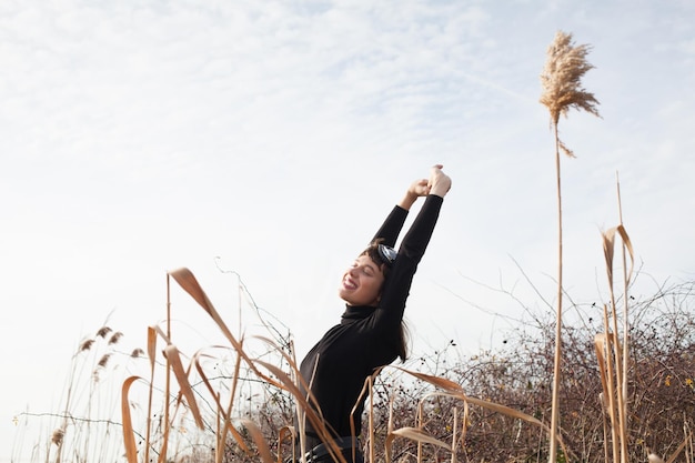 Photo smiling young woman standing with arms raised on field against sky