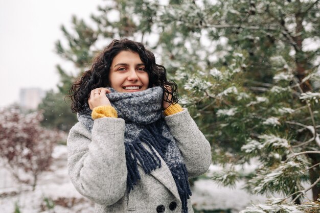 Smiling young woman stands in a frosty snowy winter park.