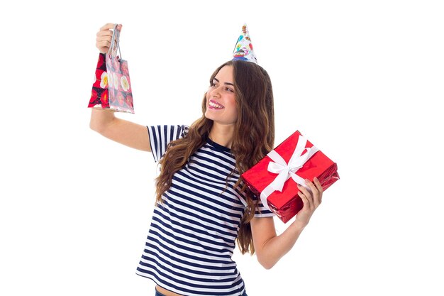 Smiling young woman in stripped Tshirt and celebration cap holding presents in studio