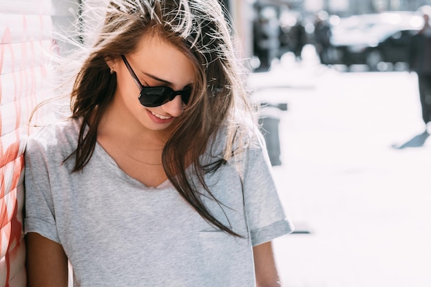 Foto giovane donna sorridente con gli occhiali da sole in piedi sul marciapiede durante una giornata di sole