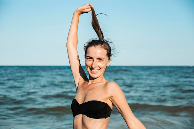 Sorridente giovane donna in costume da bagno in mare tenendo i capelli legati in una coda di cavallo.