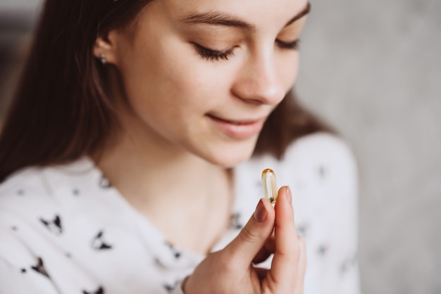 Giovane donna sorridente che prende la pillola dell'olio di fegato di merluzzo