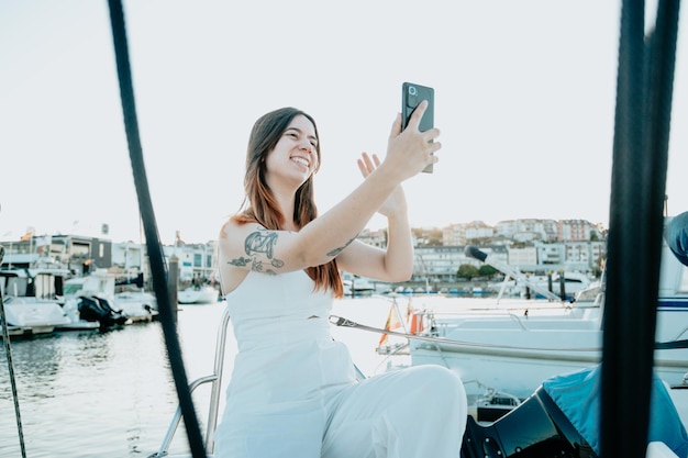 Smiling young woman taking selfies on a boat yacht sailing the sea Luxury life style conceptSmiling girl Use Social Media Streaming Service in the background yachts and ships