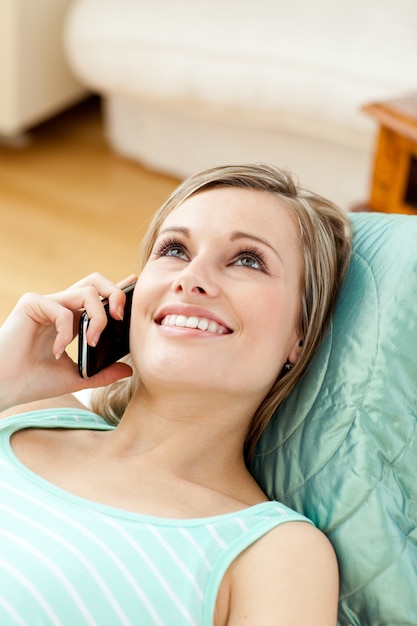 Smiling young woman talking on phone lying on a sofa