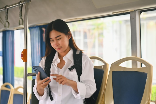 Smiling young woman text messaging on smart phone while traveling by bus Public transportation concept