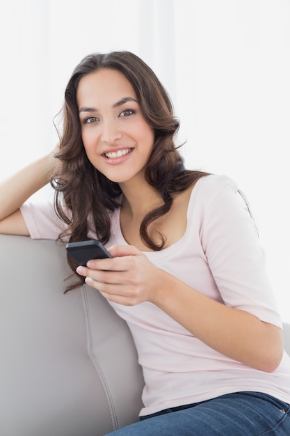 Улыбается молодая женщина текстовых сообщений на диване у себя дома