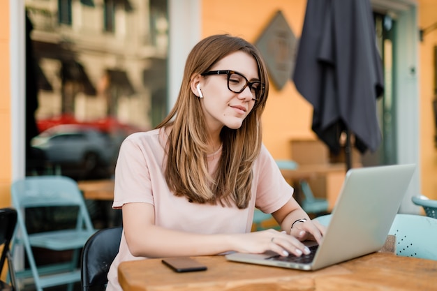 屋外のカフェでラップトップに入力する若い女性の笑みを浮かべてください。