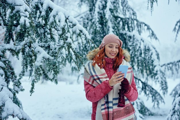 Smiling young woman typing on phone in park at cold winter day