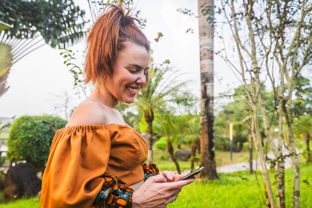 A smiling young woman uses her phone while outside