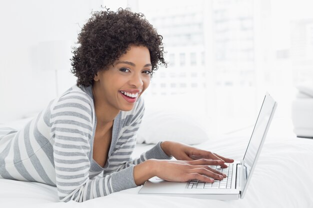 Smiling young woman using laptop in bed