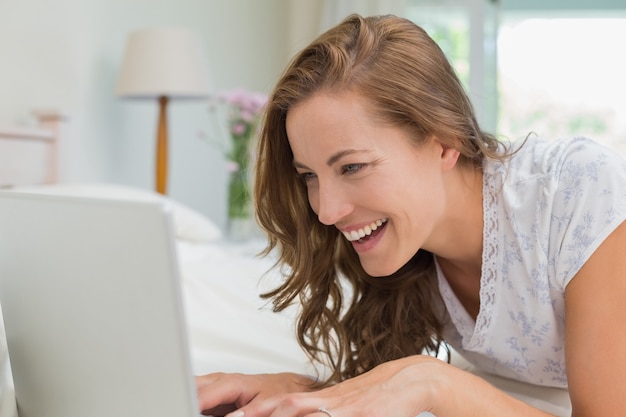 Smiling young woman using laptop in bed