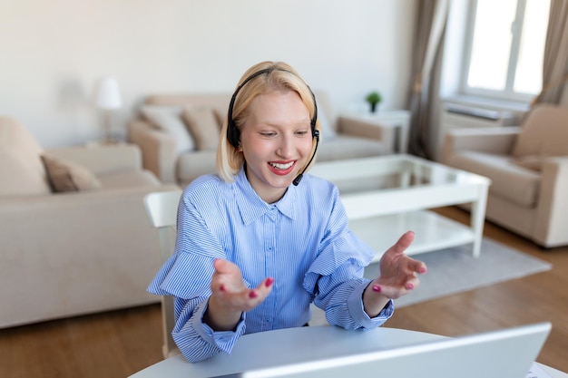 Giovane donna sorridente che utilizza il laptop a casa guardando lo schermo in chat indossando cuffie wireless con tutor aziendale in videoconferenza tramite webcam concetto di ecoaching di formazione online