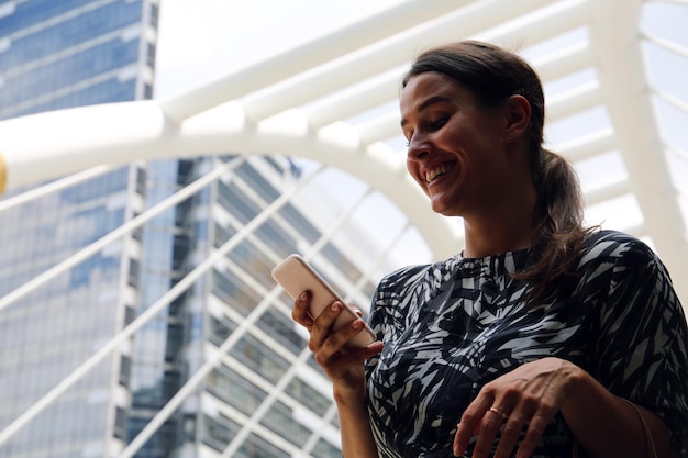 Smiling young woman using mobile phone against metallic structure