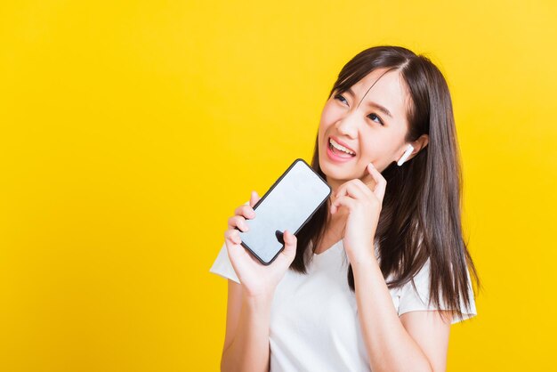 Smiling young woman using mobile phone against yellow background