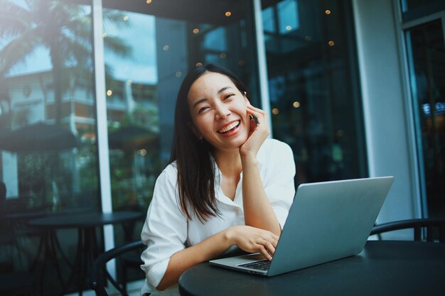 Smiling young woman using mobile phone while sitting on table