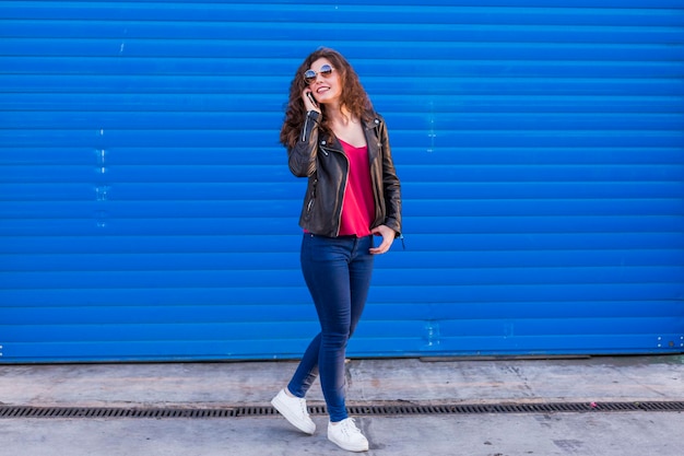 Smiling young woman using mobile phone while standing against blue wall