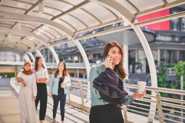 Photo smiling young woman using phone on elevated walkway in city