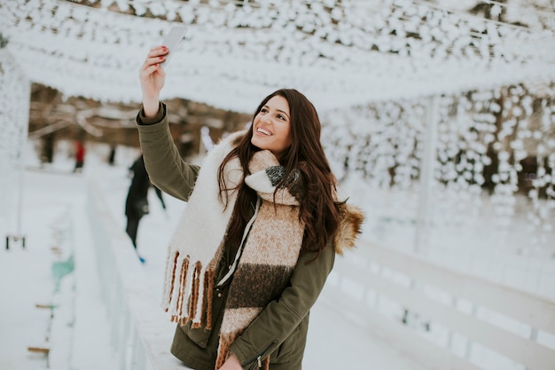 Smiling young woman using phone in park at cold winter day