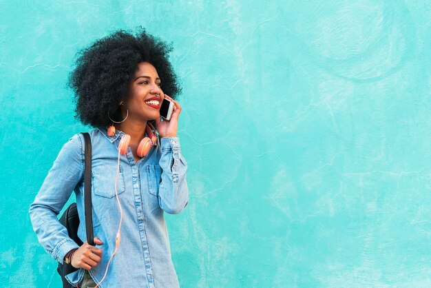 Smiling young woman using phone while standing against blue wall