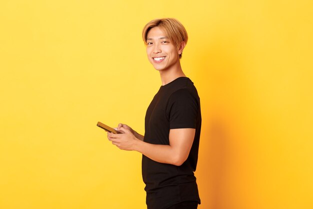 Smiling young woman using smart phone against yellow background