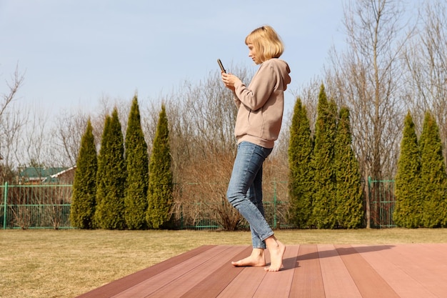 庭でスイングでリラックスしながらスマートフォンを使用して笑顔の若い女性