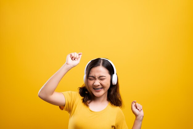 Smiling young woman wearing headphones against yellow background