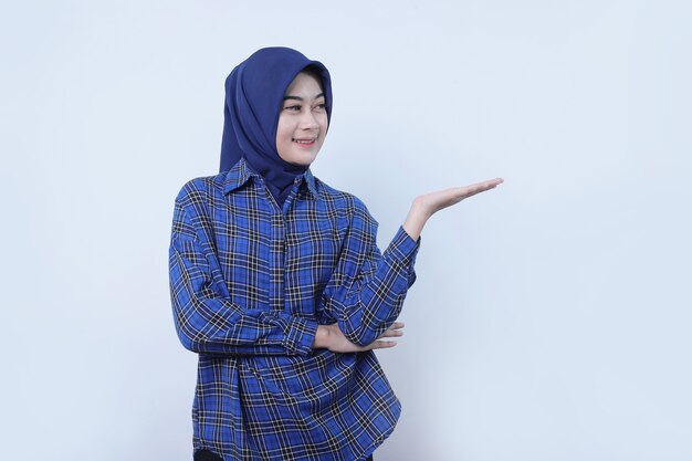 흰 벽에 격리된 손 위에 무언가를 보여주는 히잡을 쓴 웃고 있는 젊은 여성