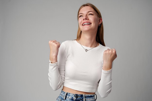 Smiling young woman in white top celebrating success with raised fist