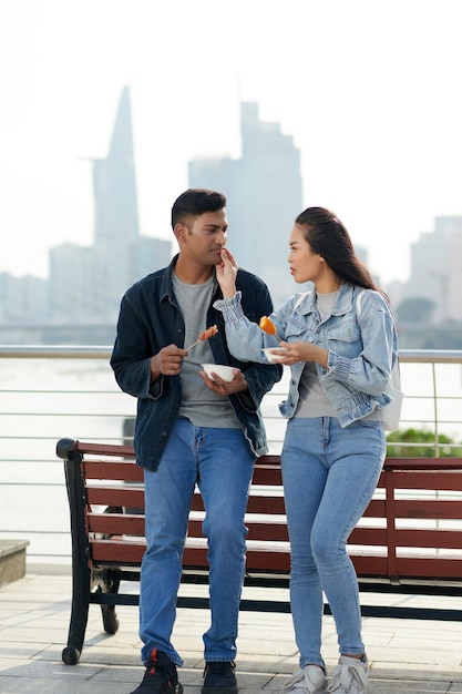 Smiling young woman wiping sauce from lips of her boyfriend when they are enjoying street food