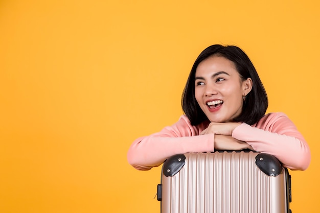 Smiling young woman with arms crossed on suitcase against yellow background