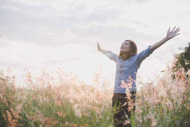 smiling young woman with arms raised standing on field against sky