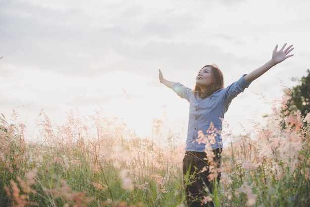 Photo smiling young woman with arms raised standing on field against sky